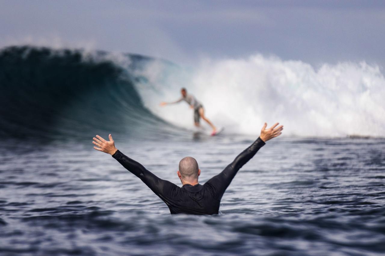 Someone in the water, both arms spread wide towards an incoming surfer